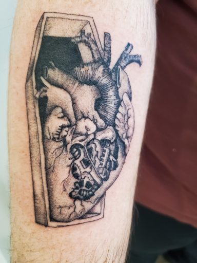 Custom mechanical fine line heart tattoo inside a coffin on a forearm.