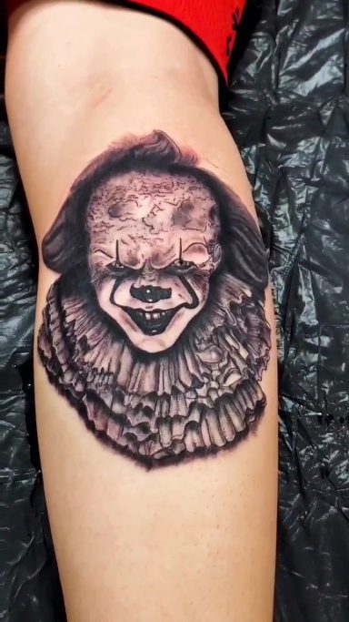 A detailed Penny wise  tattoo featuring a sinister face and frayed collar on a person's leg.