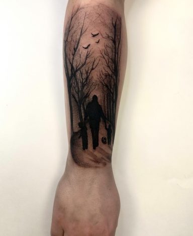 A tattoo of a silhouetted father and sons figure walking through a tree-lined path.
