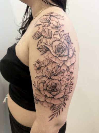 Black and grey floral tattoo featuring roses on a woman's upper arm.
