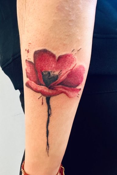 A vibrant red poppy tattoo on a person's forearm.