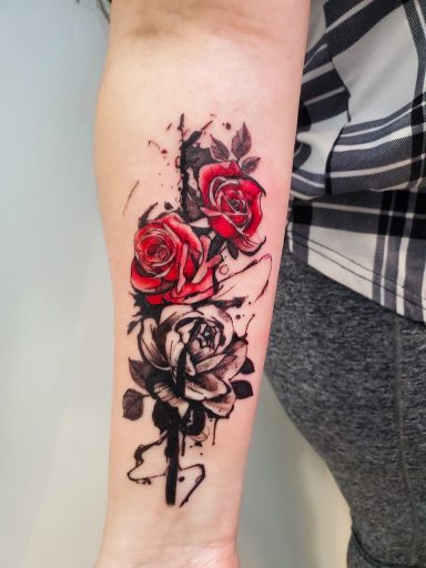 A forearm watercolour tattoo featuring two roses, one red and one grey, with artistic black detailing.