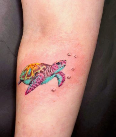 Colourful tattoo of a sea turtle swimming with bubbles on a person's arm.